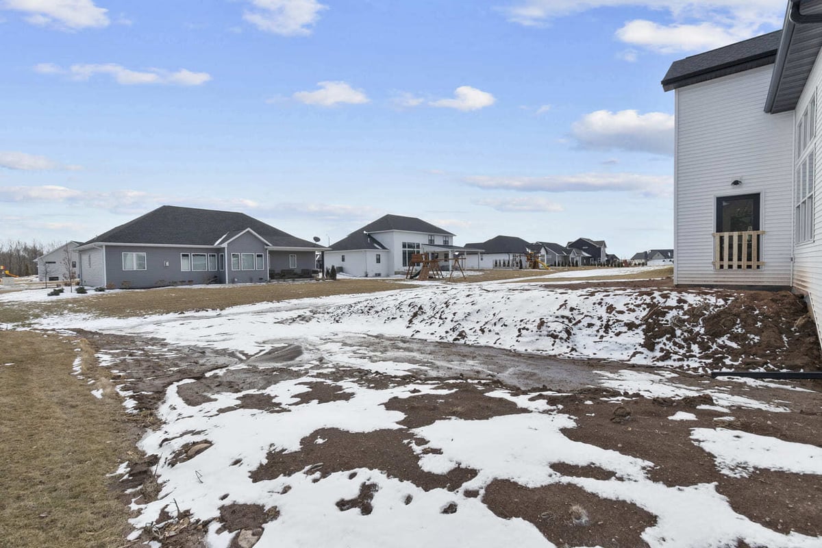 Snow-dusted side yard of a Fox Cities home with a view of surrounding houses and a playground in the distance