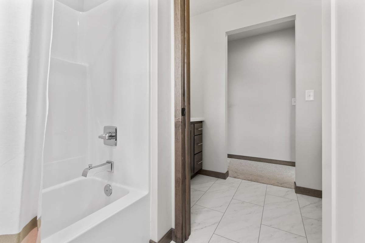White bathtub and shower combo with chrome fixtures and tile flooring in a Fox Cities bathroom