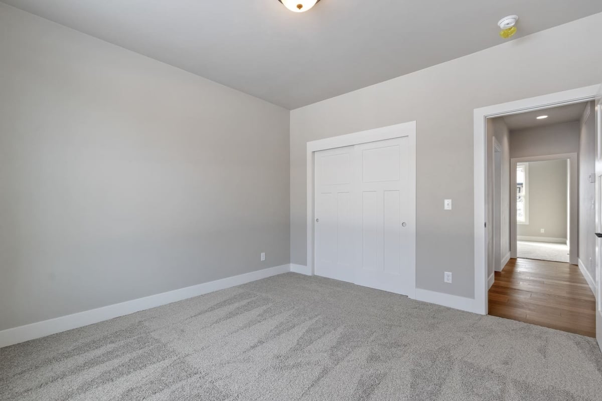 Bright carpeted bedroom with neutral walls and sliding closet doors in a newly built Fox Cities home