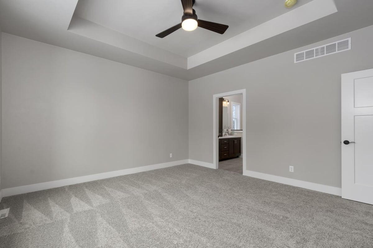 Bright primary bedroom with tray ceiling, ceiling fan, and neutral carpet in a new Fox Cities home