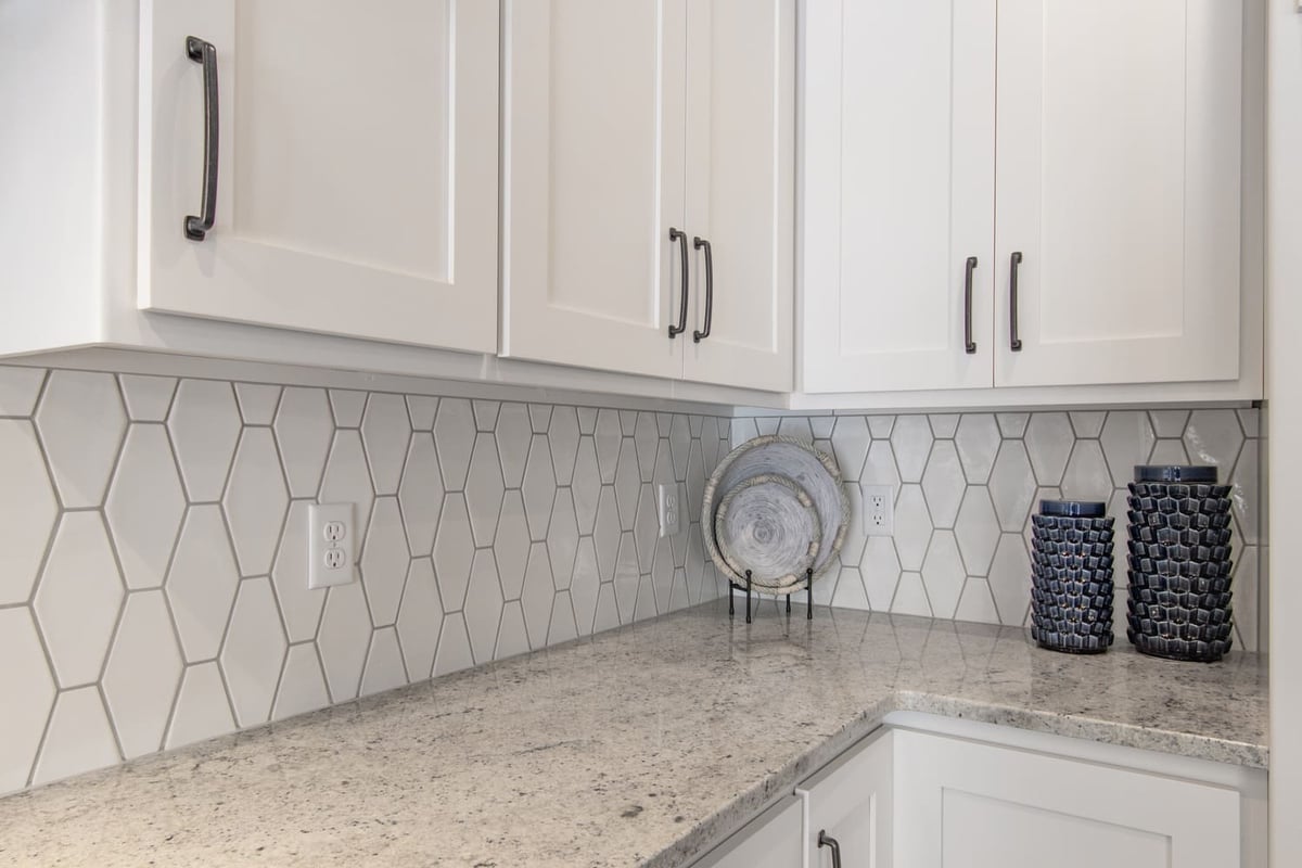 Close-up of white kitchen cabinets with hex tile backsplash and granite countertop in a Fox Cities home