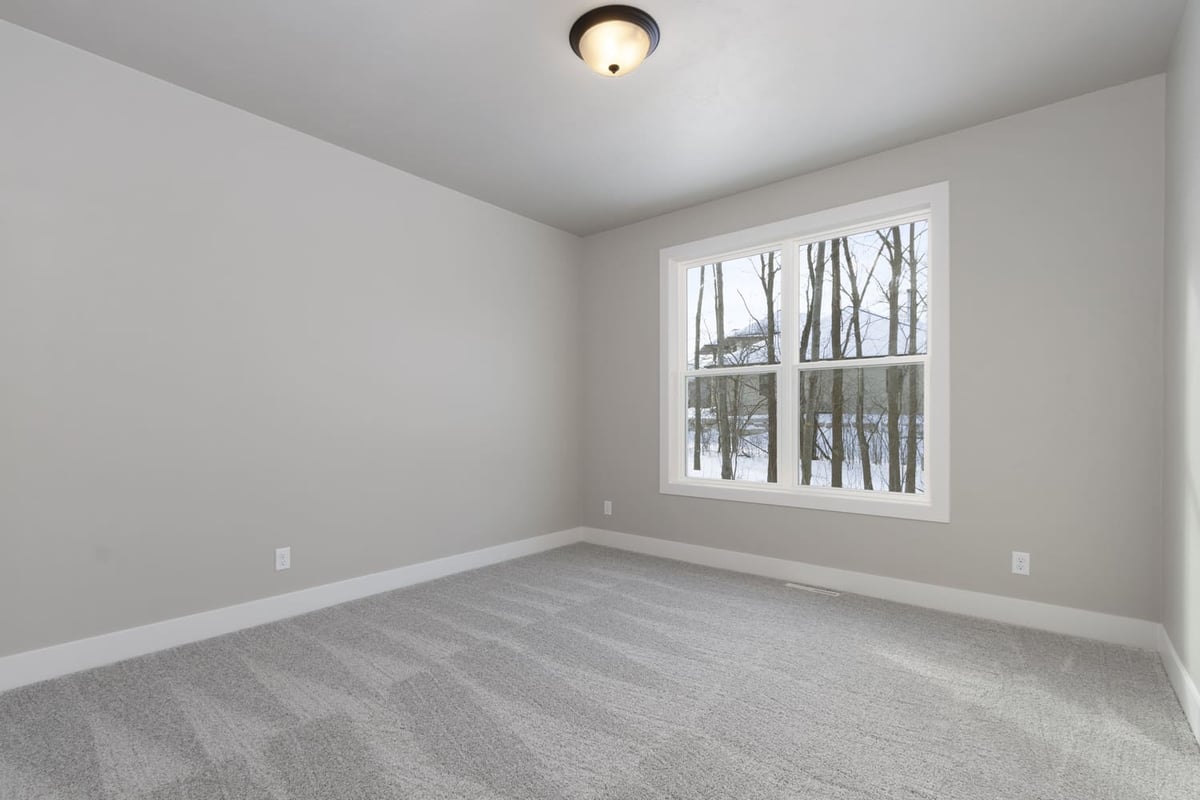 Empty bedroom with plush carpet, neutral walls, and large window overlooking trees in the Fox Cities