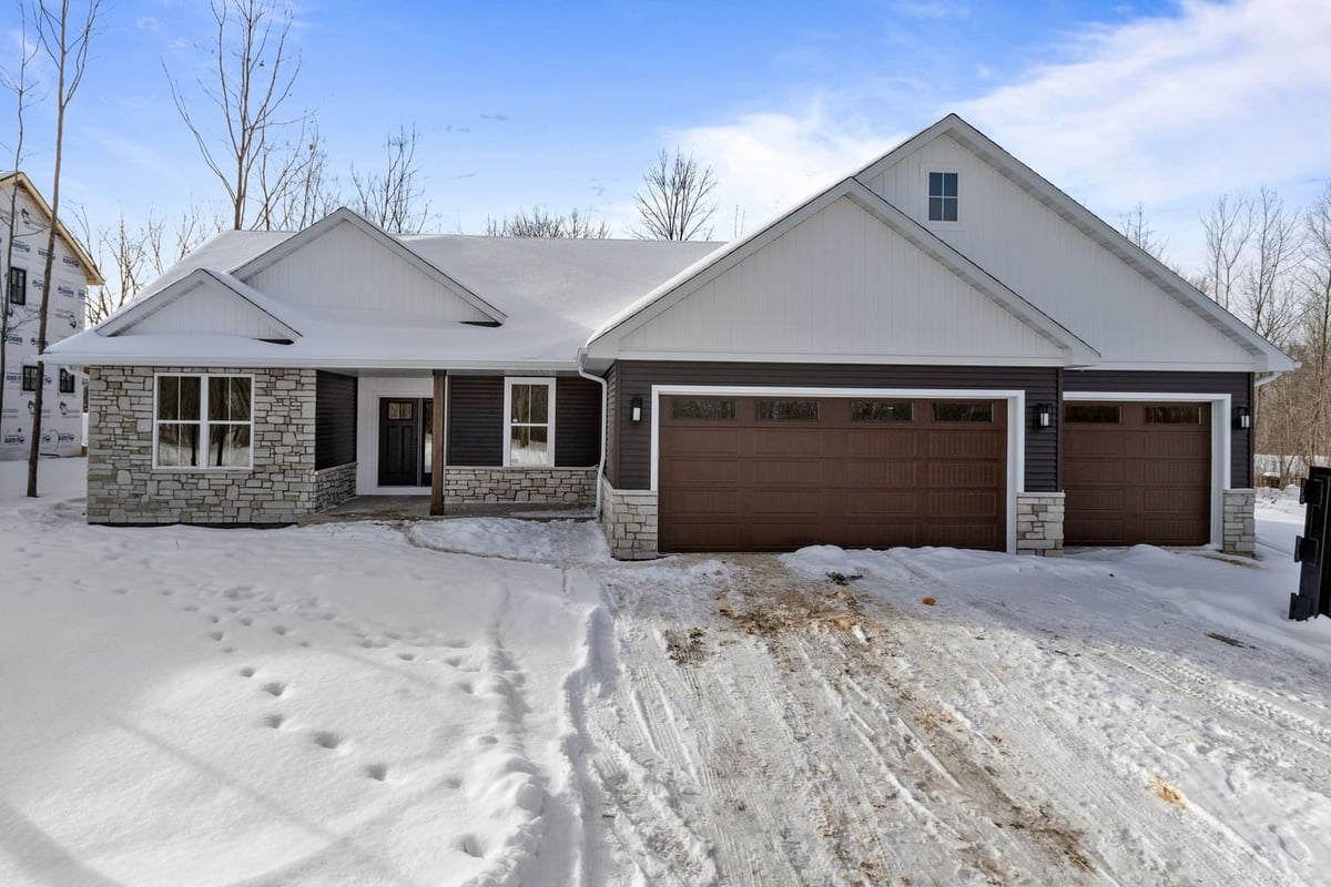 Front exterior of a modern ranch home with stone accents and three-car garage in the Fox Cities during winter