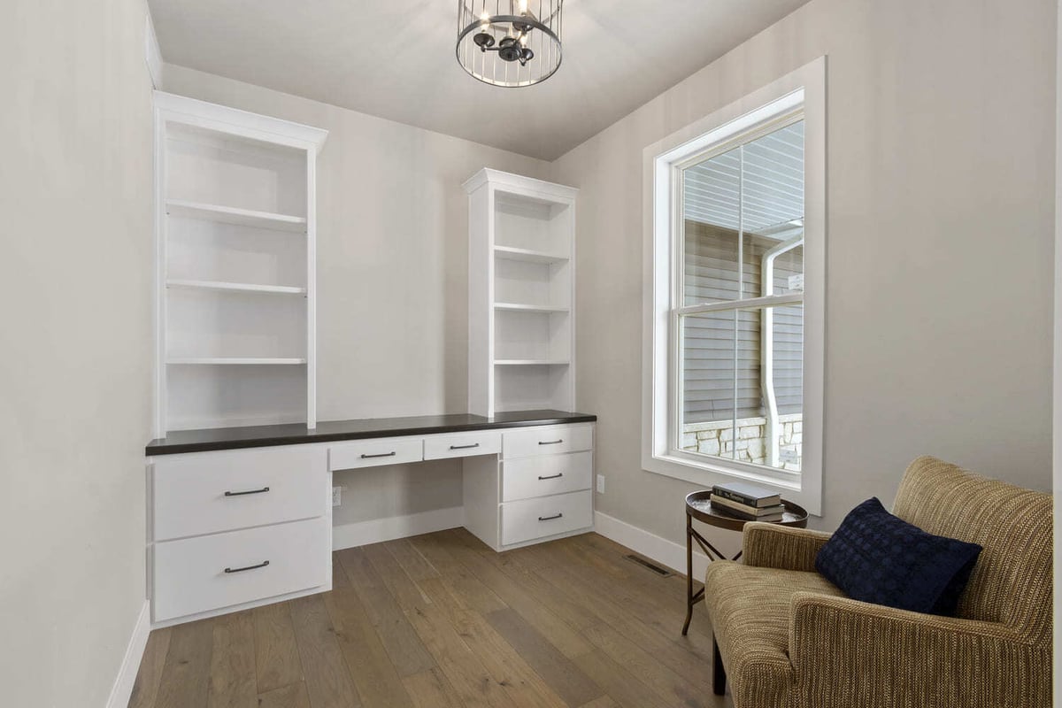Home office with built-in white shelving, desk cabinetry, wood floors, and large window in a Fox Cities home