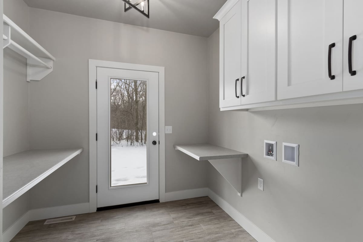 Laundry room with built-in shelving, white cabinets, and exterior door in a Fox Cities new construction home