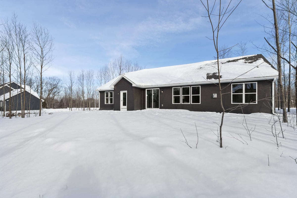 Rear exterior of a single-story home with large windows and snowy yard in a wooded Fox Cities setting