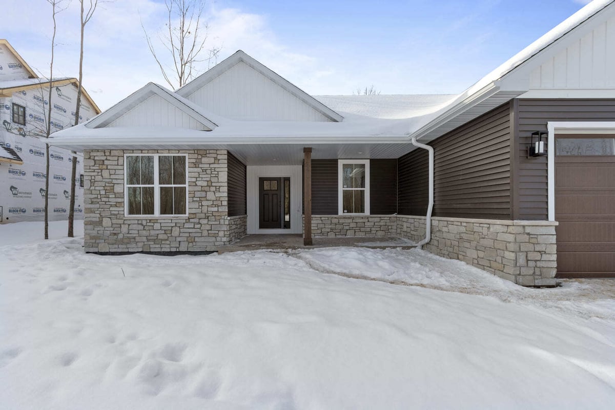 Snow-covered new construction home exterior with stone accents and covered entry, located in the Fox Cities