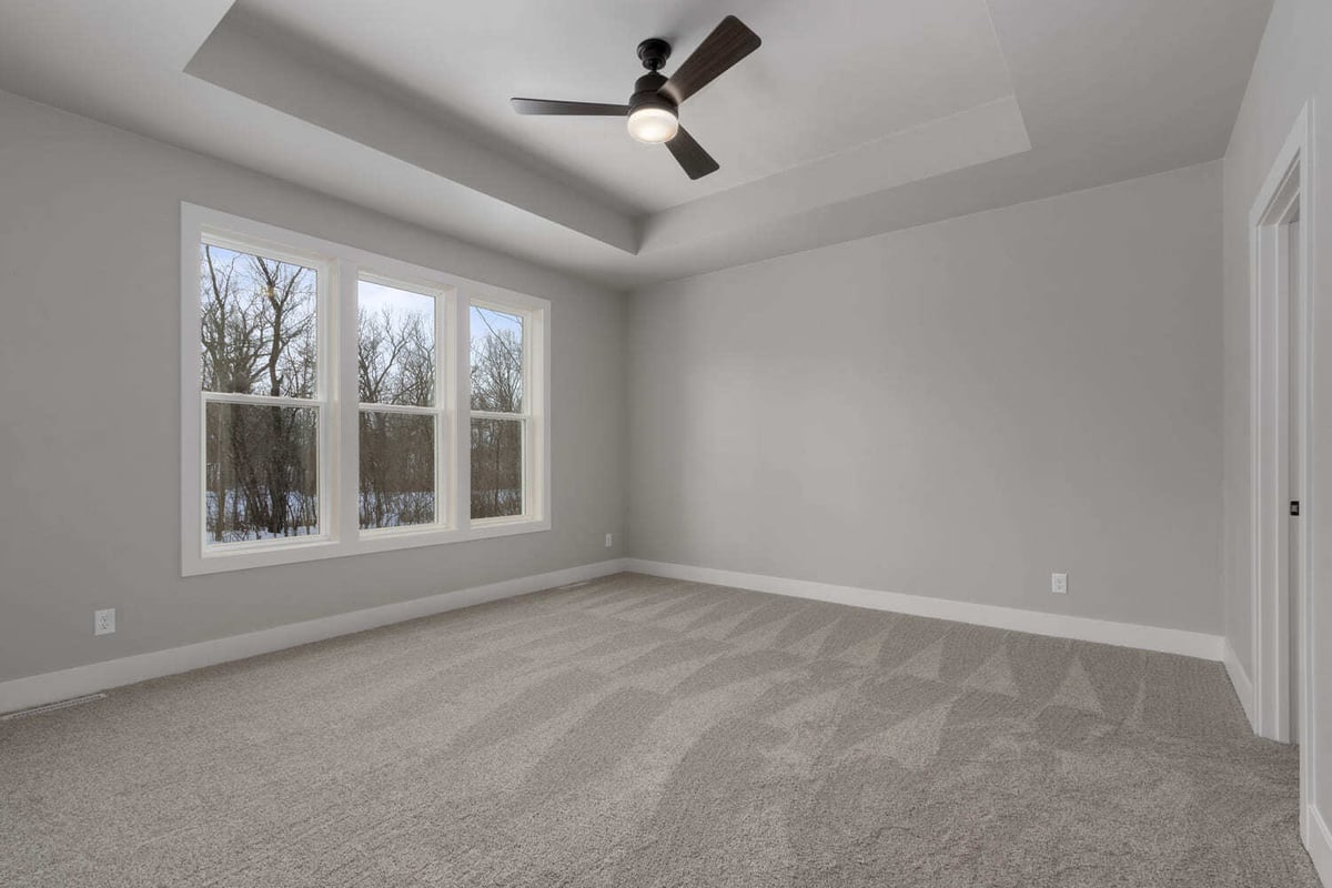 Spacious bedroom with large windows, tray ceiling, and soft carpet in a Fox Cities new construction home