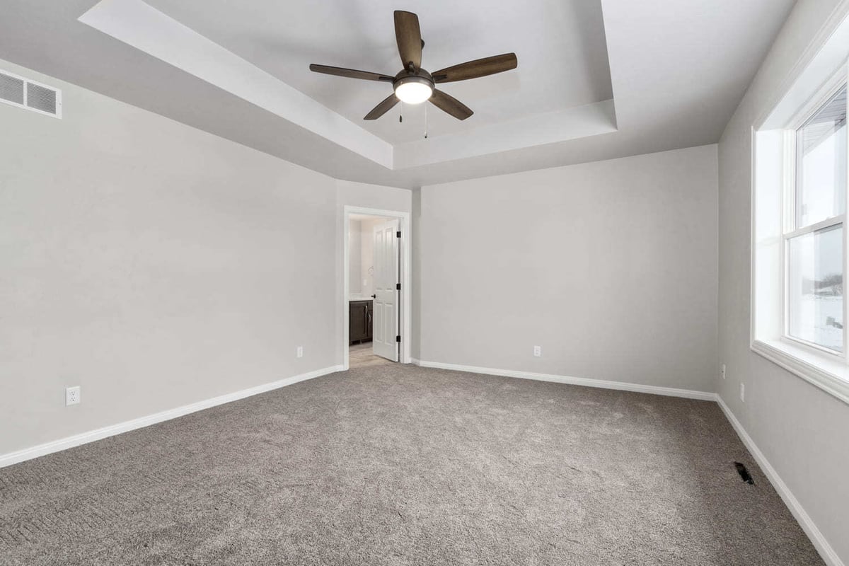 Empty bedroom with tray ceiling, ceiling fan, carpeted floor, and neutral walls in the Fox Cities
