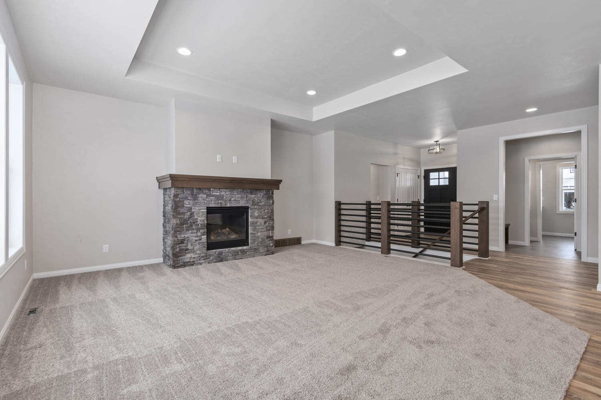 Open living room with stone fireplace, tray ceiling, and carpeted floor in a Fox Cities home