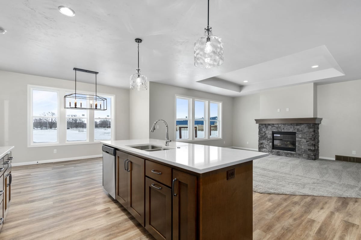 Open-concept kitchen and living area with large island, pendant lights, and stone fireplace in the Fox Cities