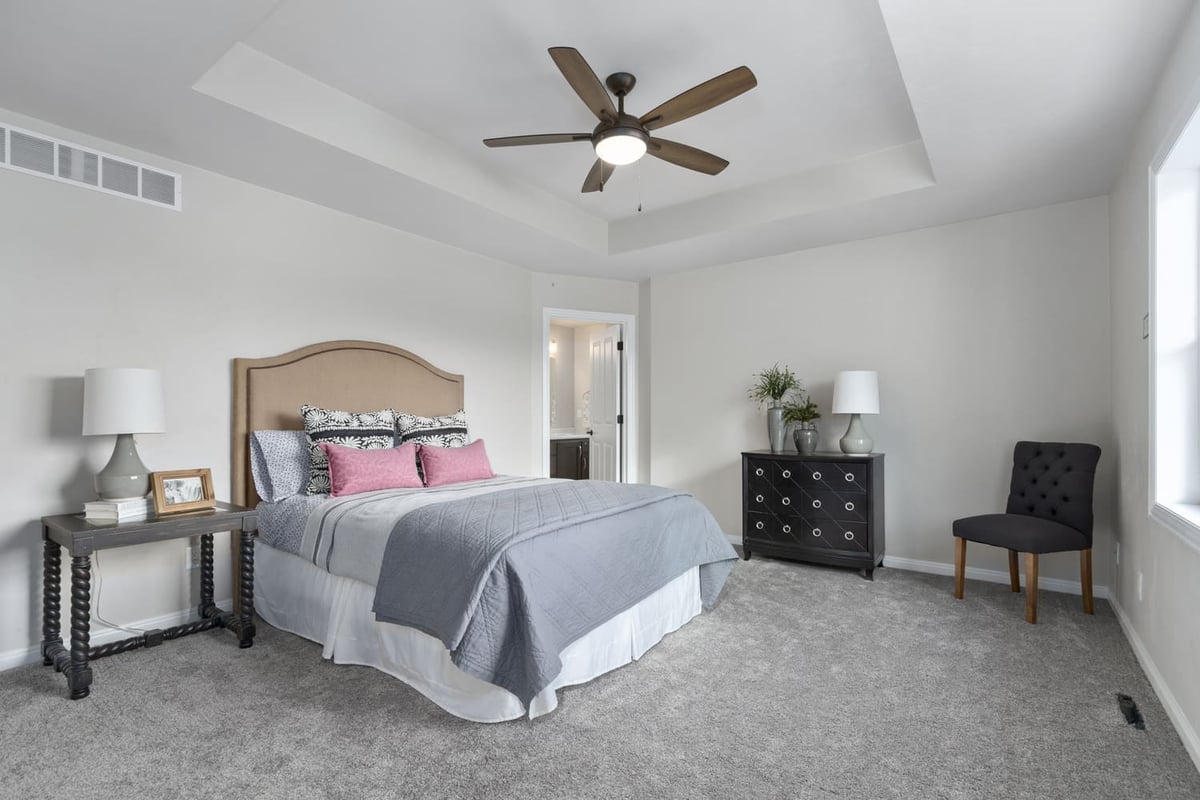 Primary bedroom with tray ceiling, ceiling fan, staged bed, and neutral finishes in a Fox Cities home