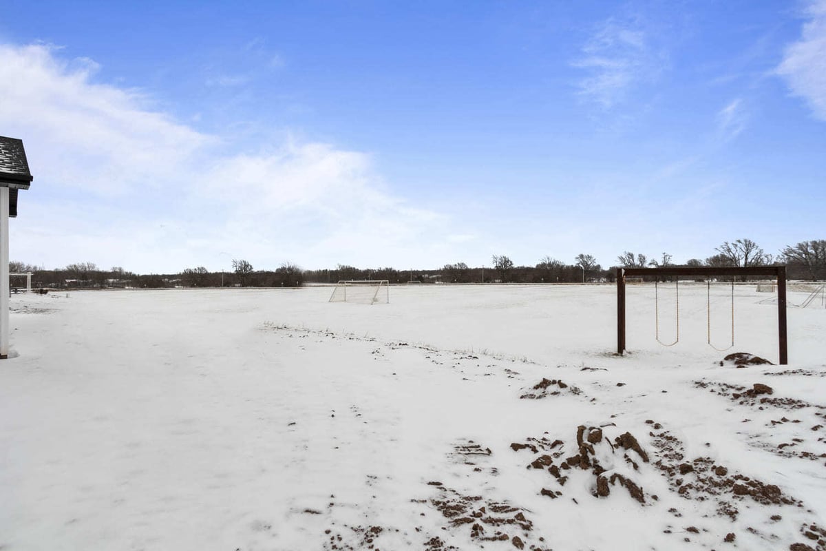 Snow-covered backyard with open field and playset behind a Fox Cities home