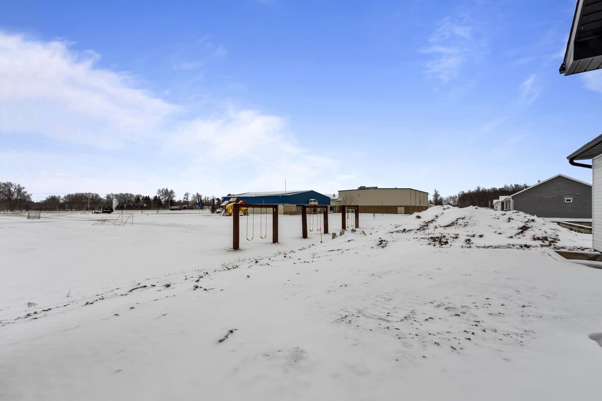 Snow-covered backyard with open space and playset behind a Fox Cities home