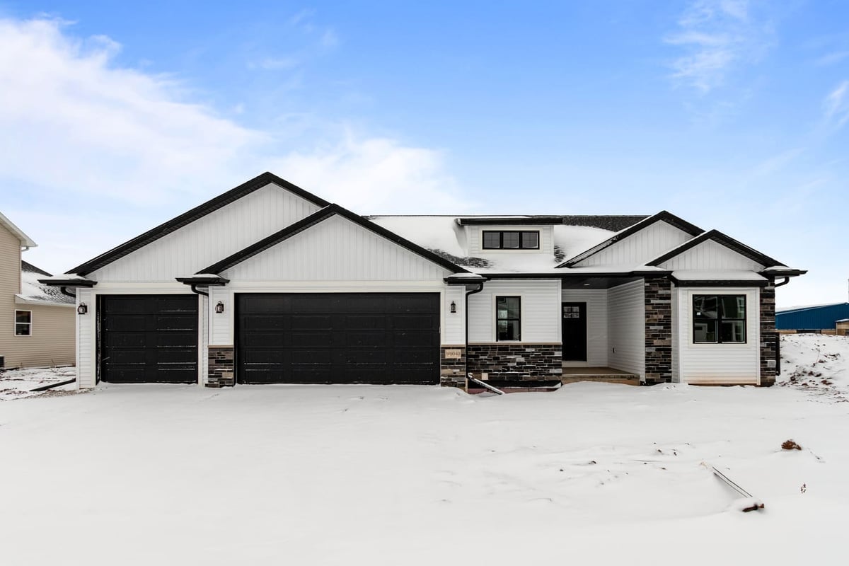 Snow-covered exterior of a modern single-story home with black garage doors in the Fox Cities