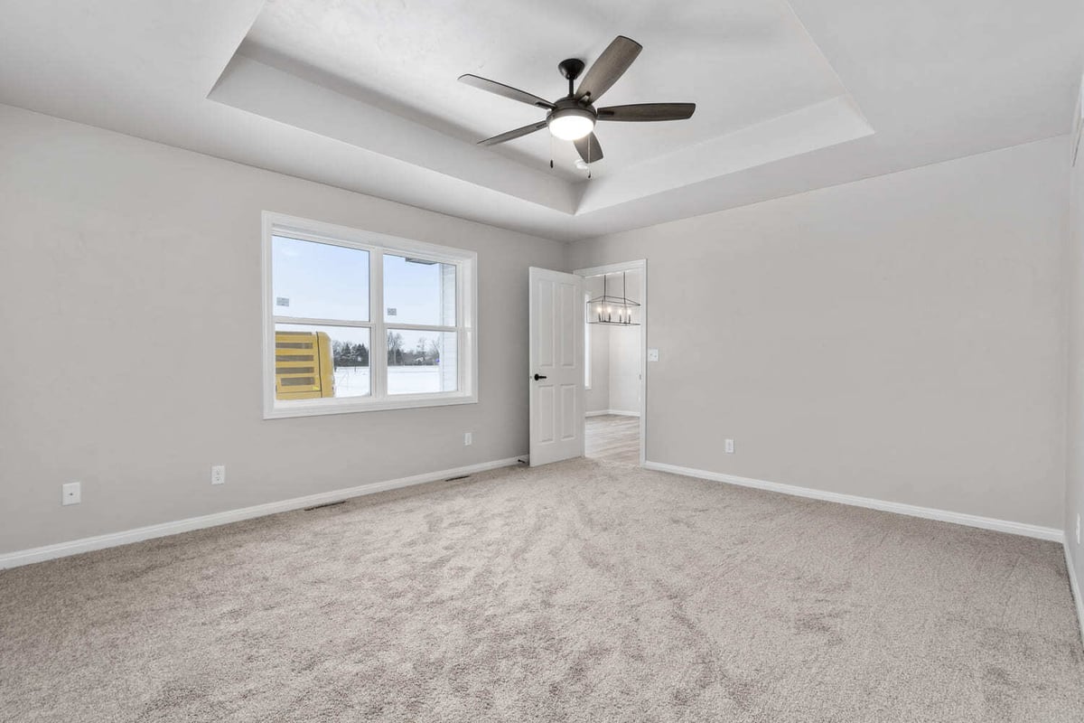 Unfurnished primary bedroom with tray ceiling, ceiling fan, carpeted floor, and window in a Fox Cities home