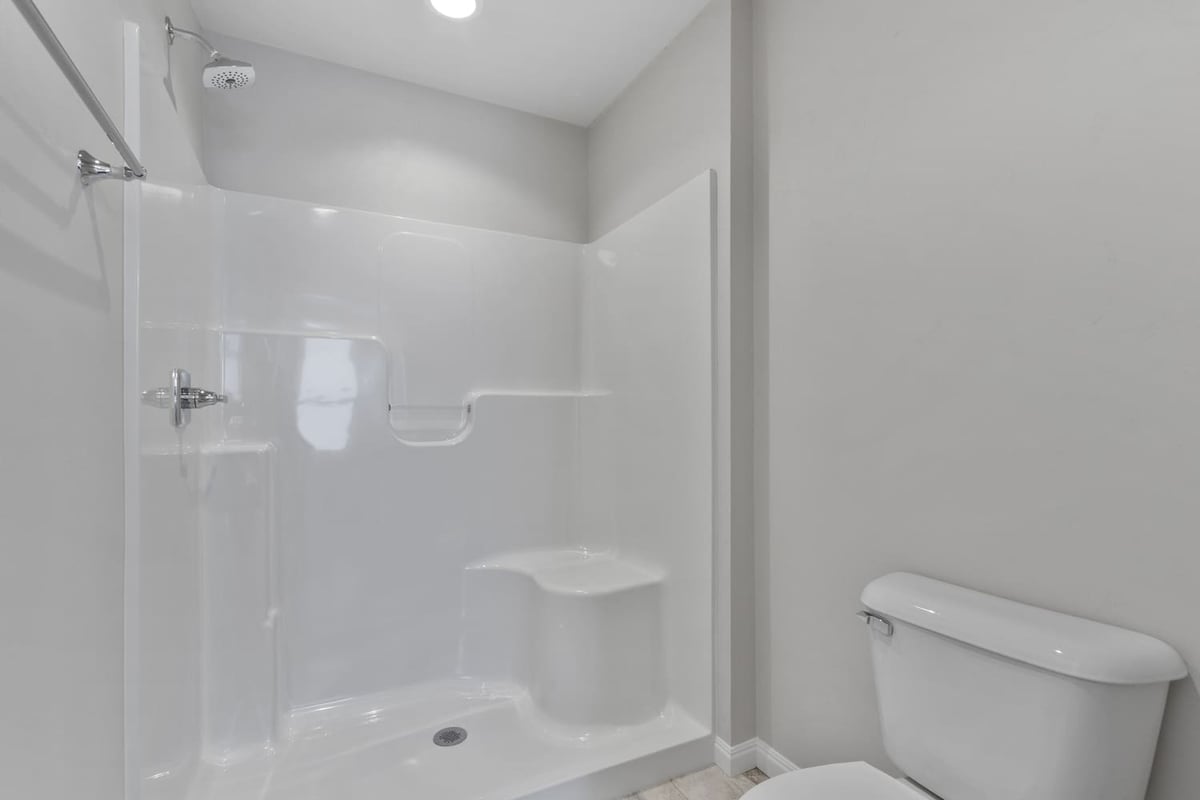 Walk-in shower with built-in bench, white surround, and modern fixtures next to toilet in a Fox Cities home