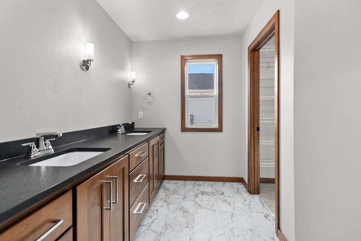 Bathroom vanity with dual sinks, marble-look tile floor, and walk-in closet access, located in the Fox Cities