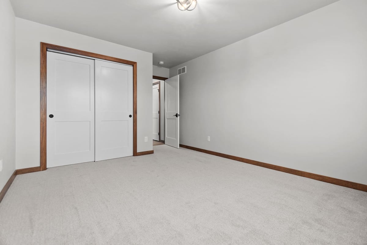 Bedroom with sliding closet doors, carpet flooring, and wood trim in a home located in the Fox Cities