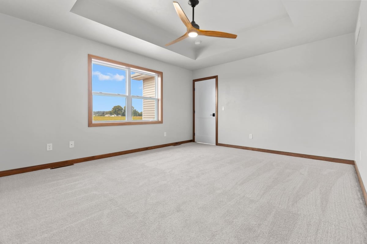 Bright bedroom with tray ceiling, ceiling fan, neutral carpet, and large window in a Fox Cities home