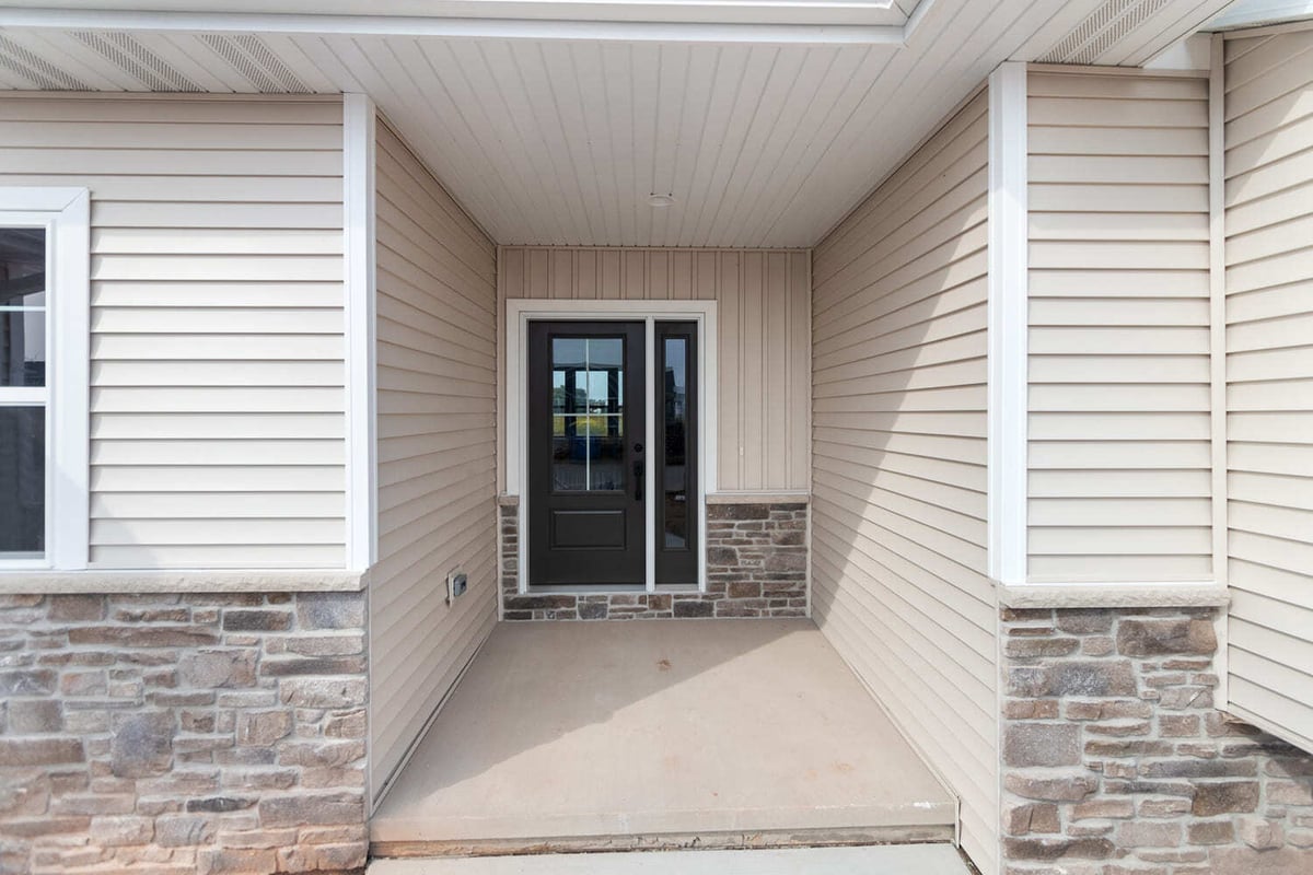 Covered front porch with stone details, beige siding, and glass front door in the Fox Cities