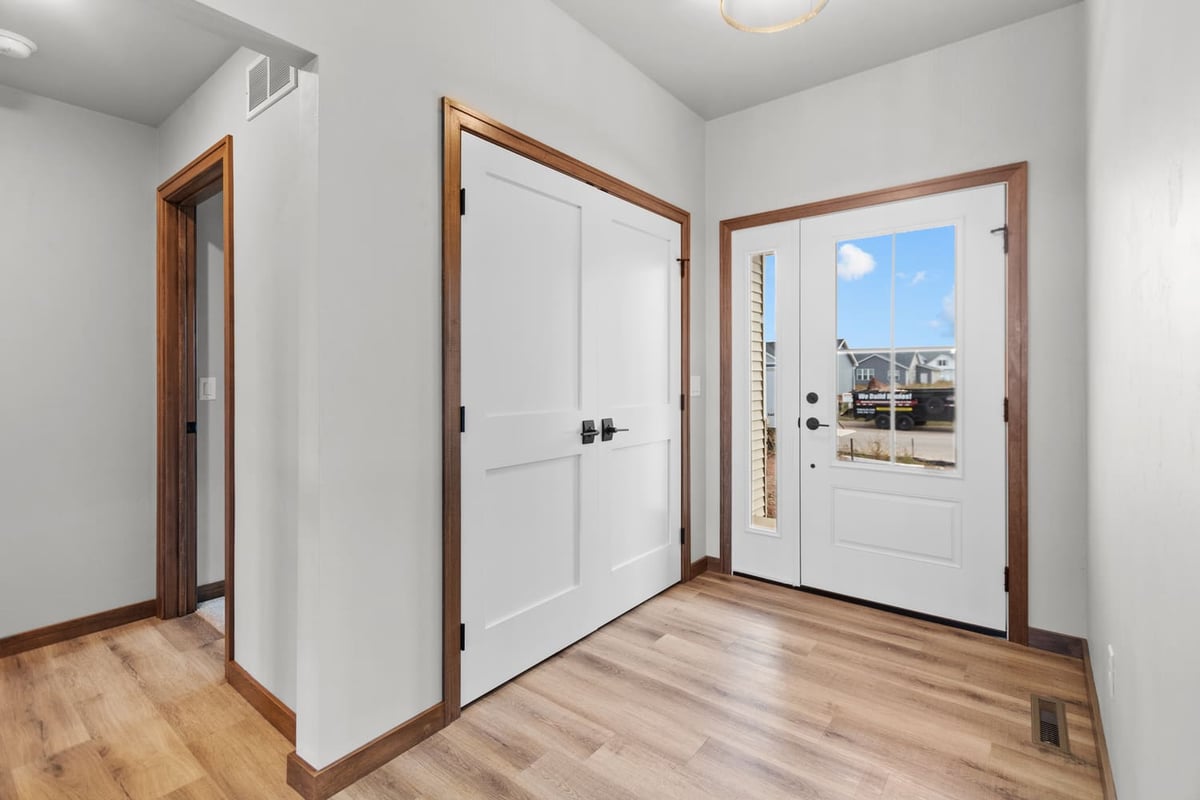 Entryway with double front doors, wood-look flooring, and closet storage in a new home located in the Fox Cities