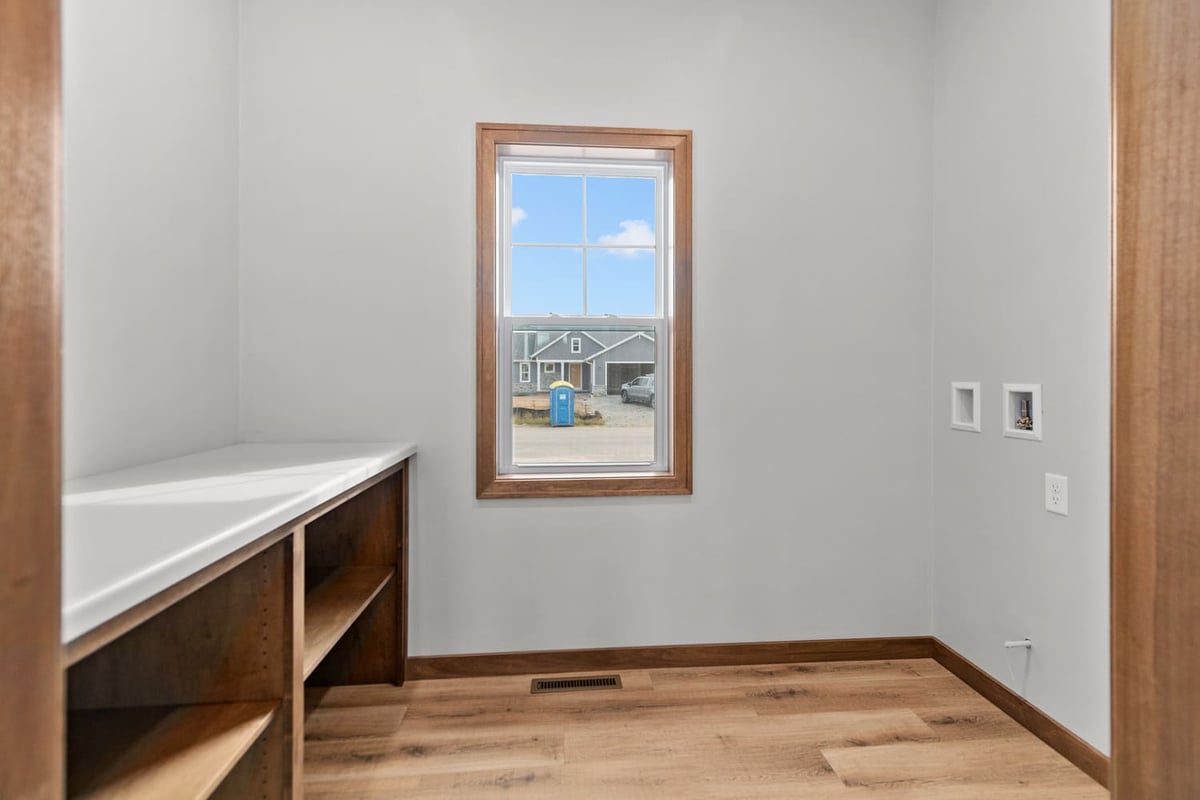 Laundry room with built-in shelving, countertop workspace, window, and wood-look flooring in a home located in the Fox Cities