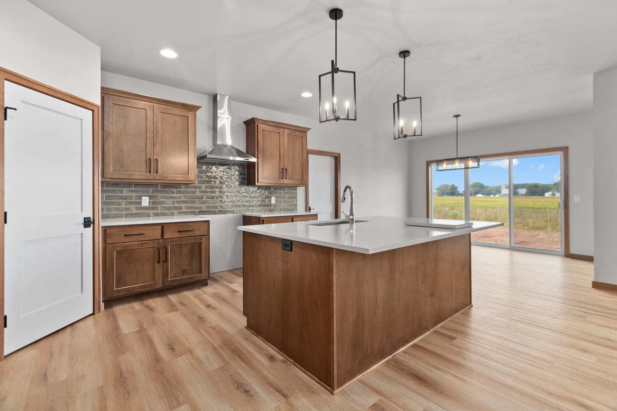Modern kitchen with wood cabinets, large island, pendant lights, and sliding doors to backyard in a Fox Cities home