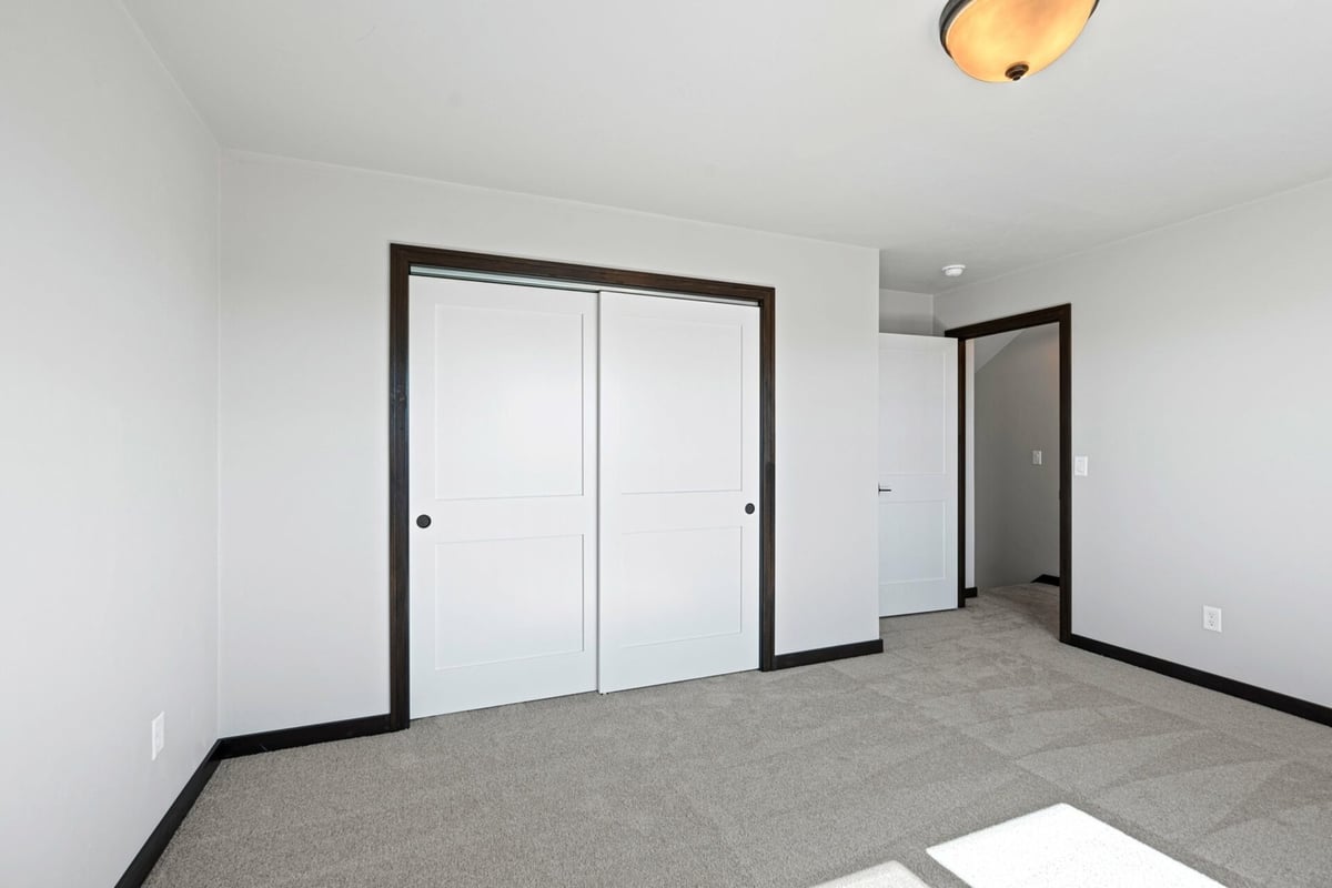 Carpeted bedroom with dual sliding closet doors in a custom home by Midwest Design Homes in Fox Cities, WI.