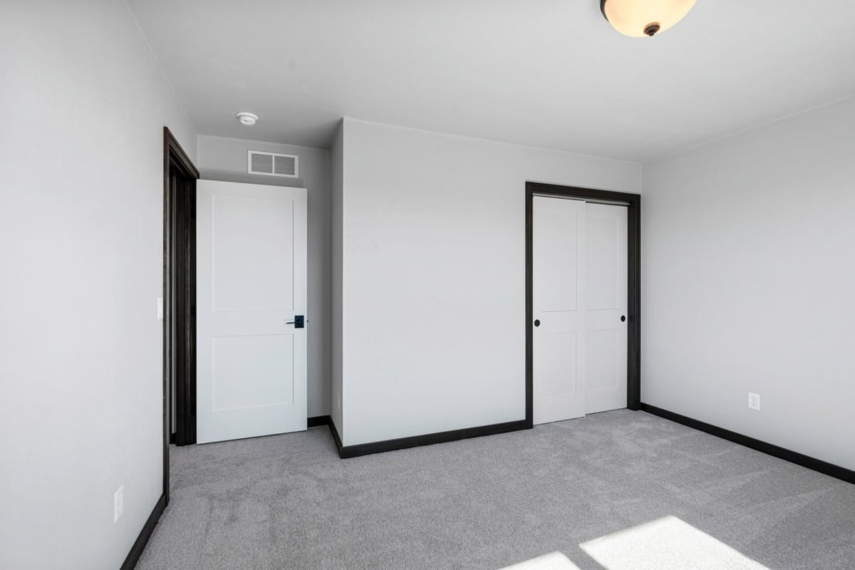 Custom home bedroom featuring white trim, carpet, and modern closet by Midwest Design Homes in Ellington, WI.