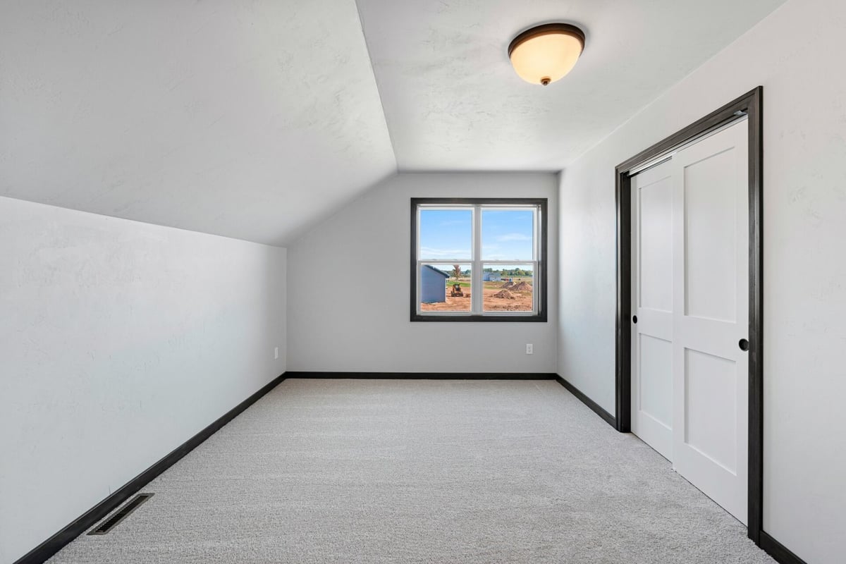 Sloped ceiling bedroom with soft carpet and large window in a custom home by Midwest Design Homes in De Pere, WI.