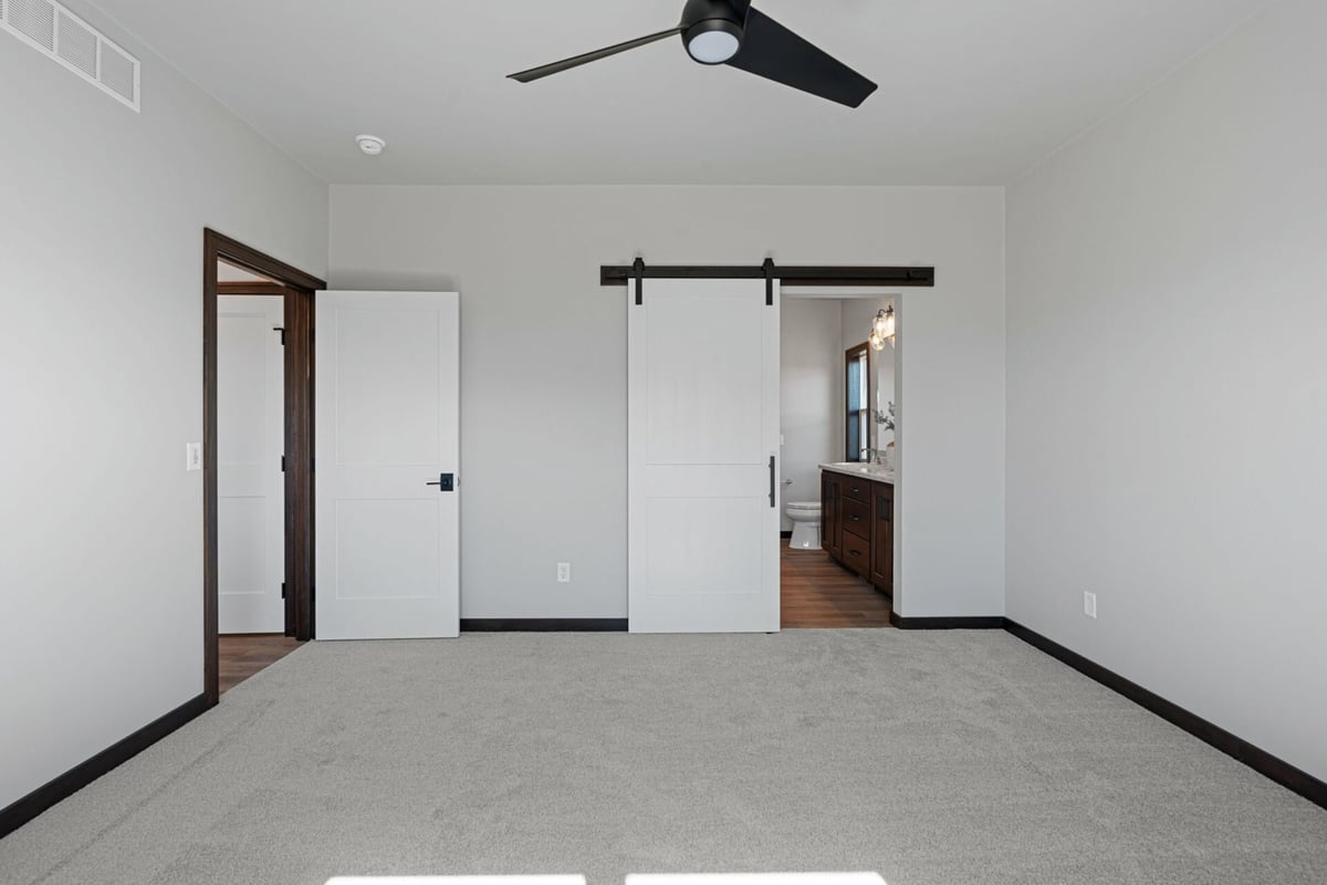 Spacious bedroom with barn door leading to en-suite bathroom in a custom home by Midwest Design Homes in Neenah, WI.