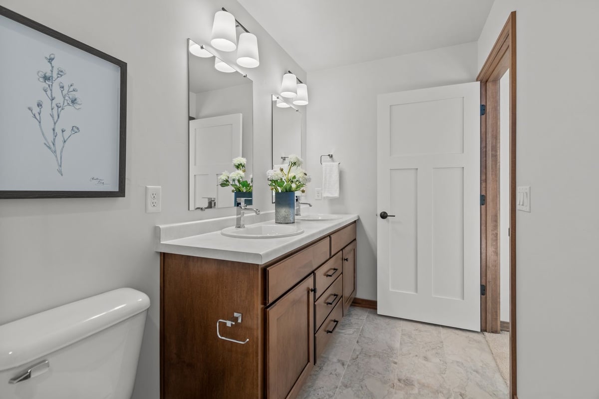 Bathroom with double vanity, mirrors, and modern lighting, featuring wood cabinetry and tile floor, located in the Fox Cities