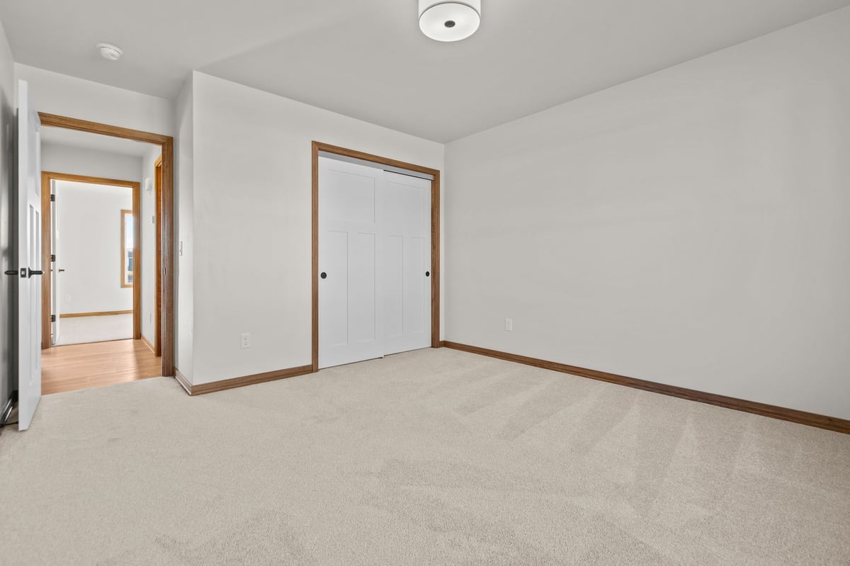 Empty bedroom with carpet flooring, double closet doors, and hallway view, located in the Fox Cities