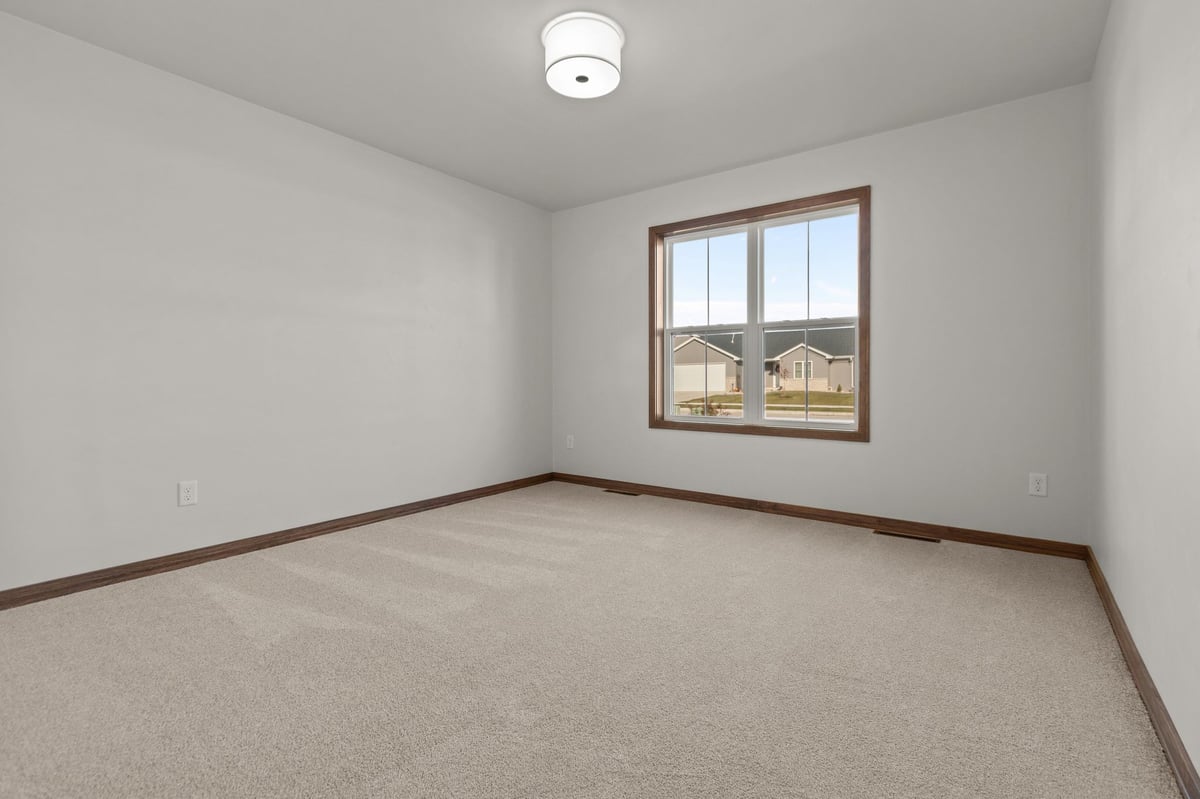 Empty bedroom with carpet flooring, neutral walls, and large window overlooking a neighborhood, located in the Fox Cities