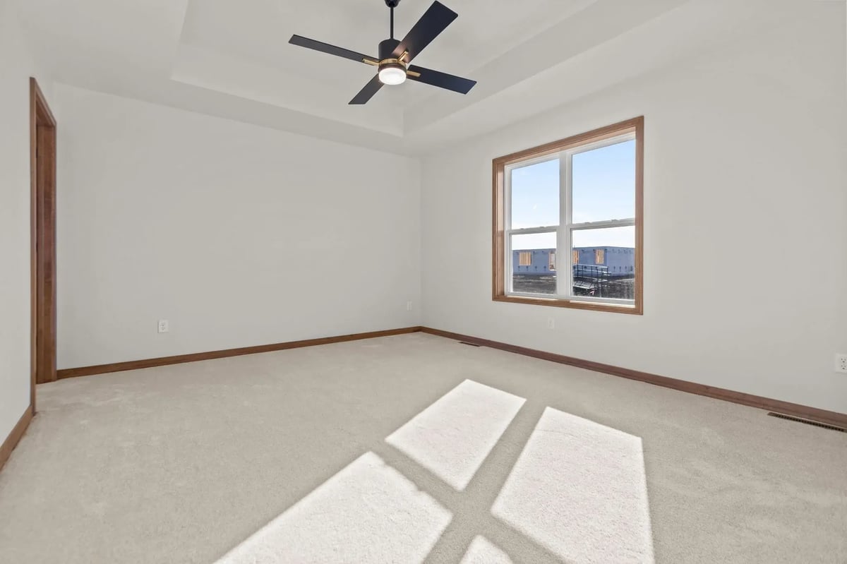 Empty bedroom with carpeted floors, tray ceiling, ceiling fan, and large window, located in the Fox Cities