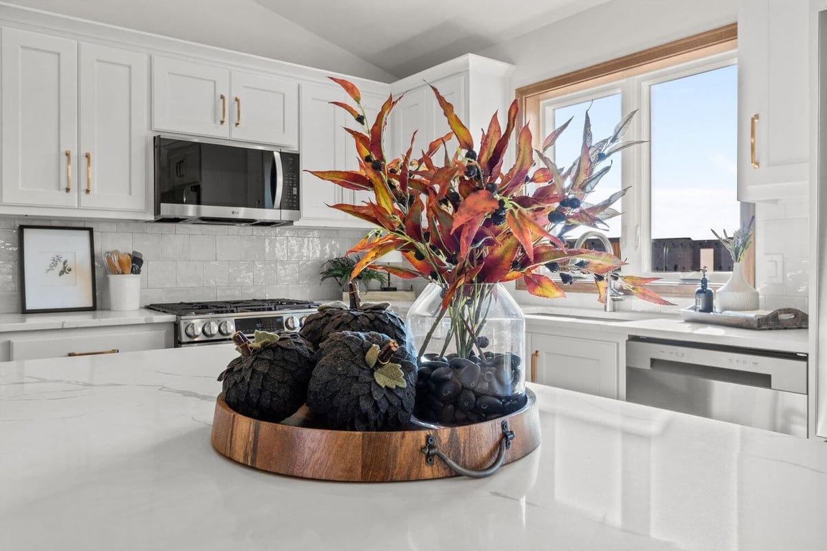 Kitchen island with quartz countertop, white cabinets, stainless appliances, and fall decor centerpiece in a bright Fox Cities home