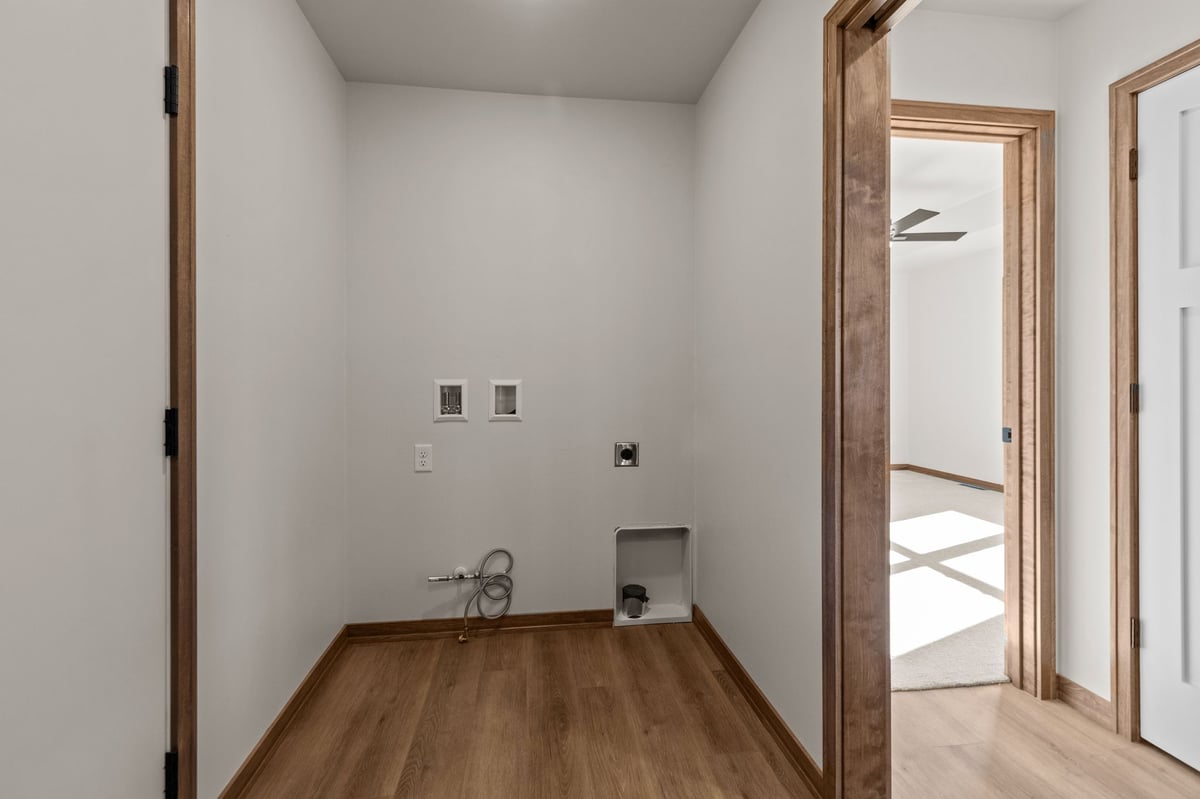 Laundry room with washer and dryer hookups, wood-look flooring, and doorway to bedroom, located in the Fox Cities