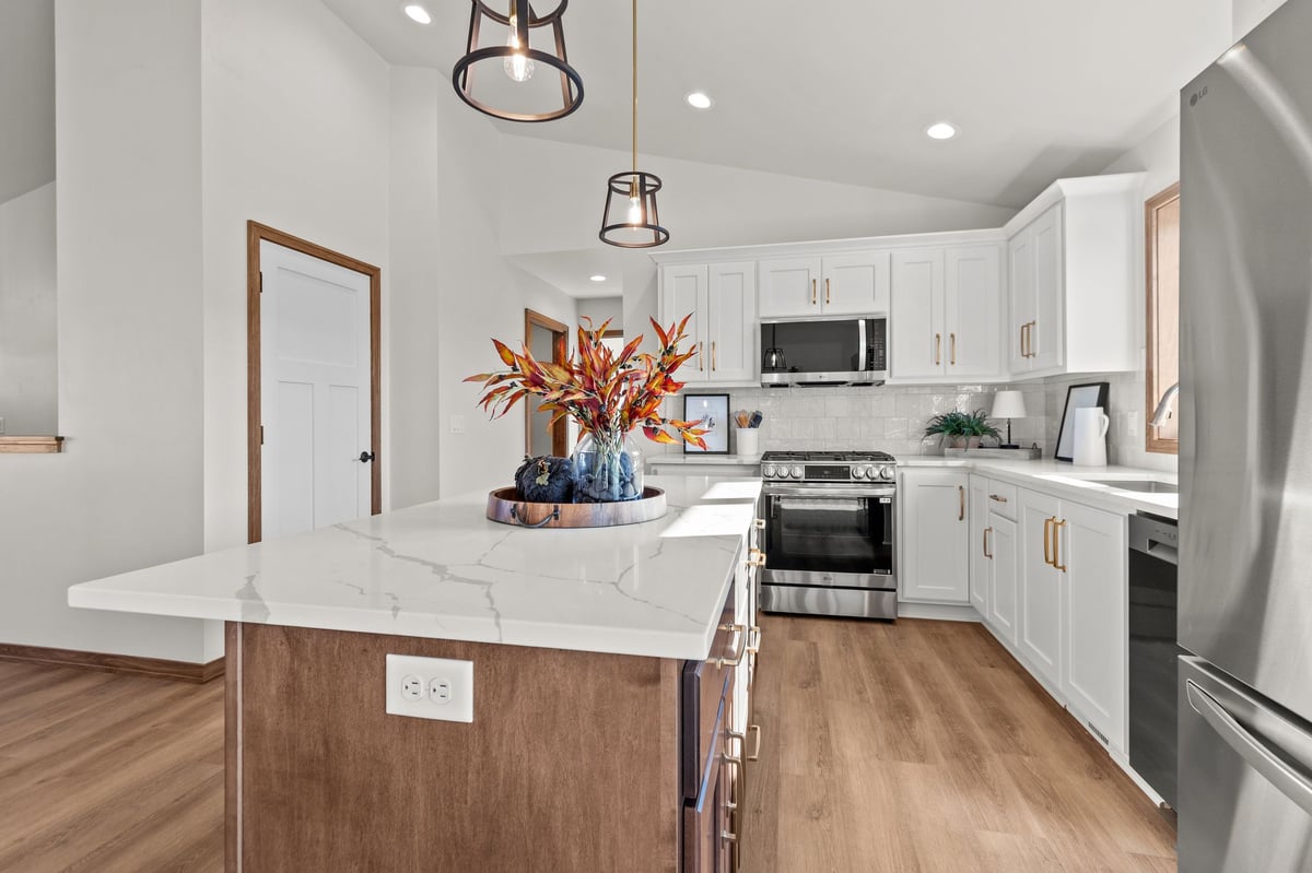 Modern kitchen with white cabinets, quartz island, pendant lights, and stainless appliances, located in the Fox Cities