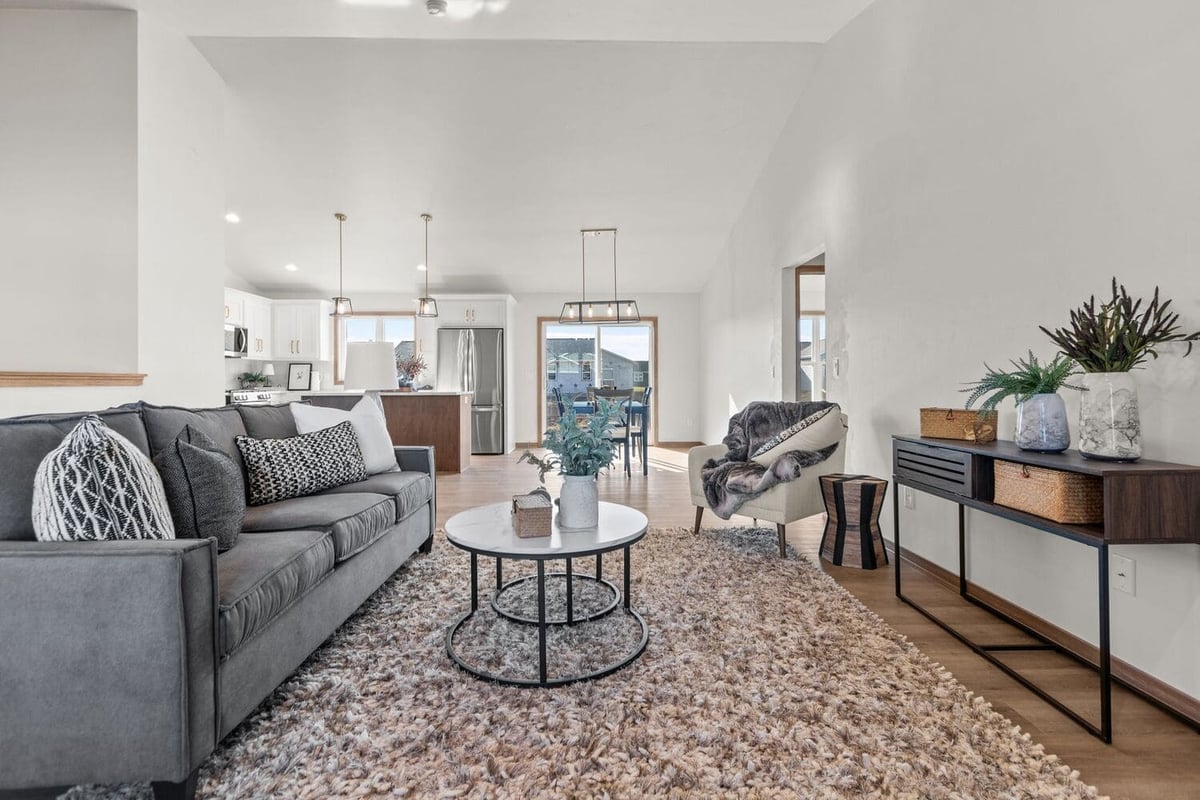 Open-concept living room with sofa, accent chair, area rug, and kitchen view in a modern home located in the Fox Cities