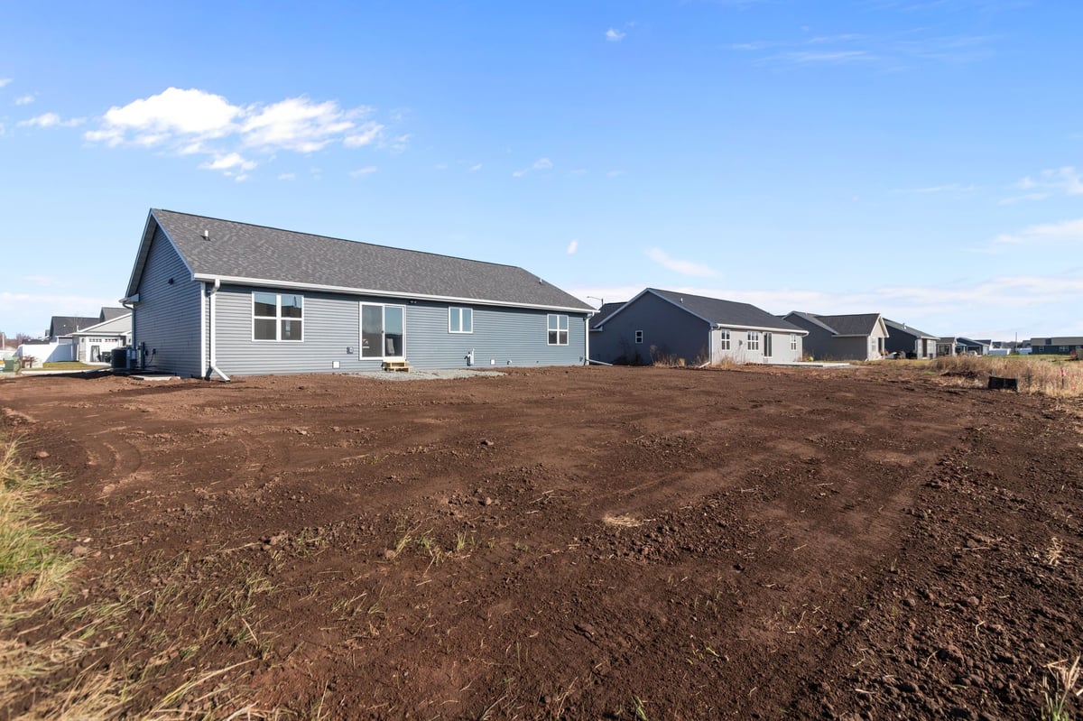 Rear view of a newly built home with unfinished yard and neighboring houses, located in the Fox Cities