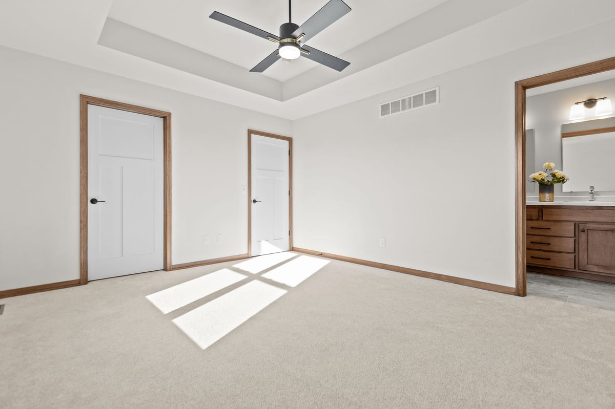 Spacious bedroom with tray ceiling, ceiling fan, carpeted floors, and ensuite bath, located in the Fox Cities