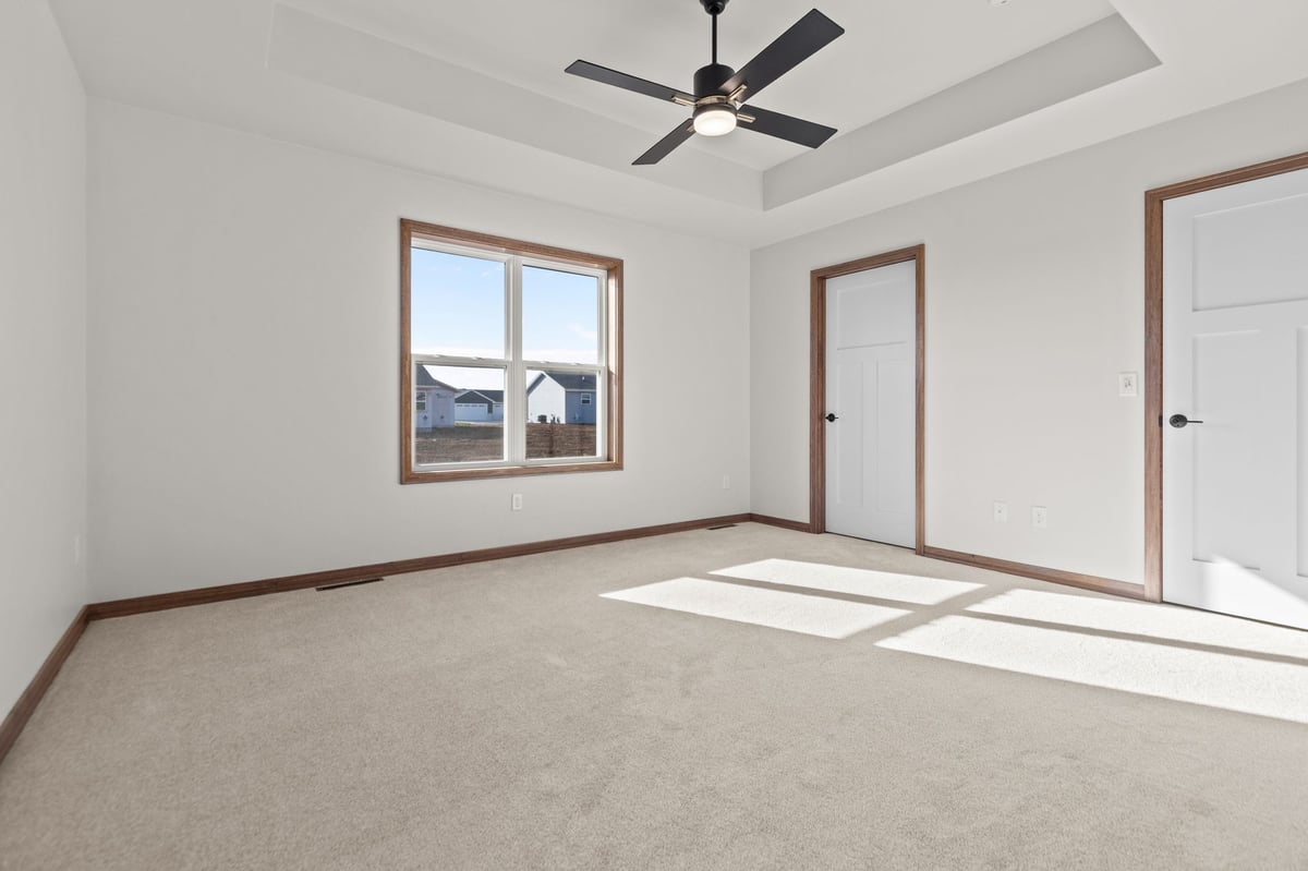 Spacious bedroom with tray ceiling, ceiling fan, large window, and carpeted floors, located in the Fox Cities