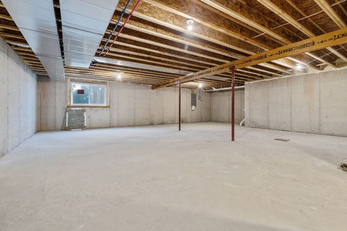 Unfinished basement with concrete floors, support beams, exposed ductwork, and egress window, offering future living space potential in the Fox Cities