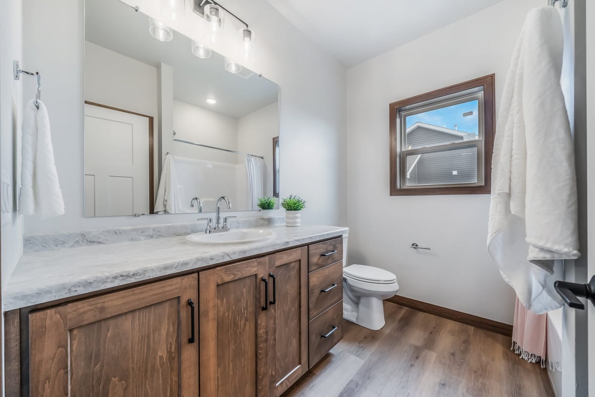 Guest bathroom with large mirror, wood cabinetry, and bright window in custom home by Midwest Design Homes in Fox Cities, WI