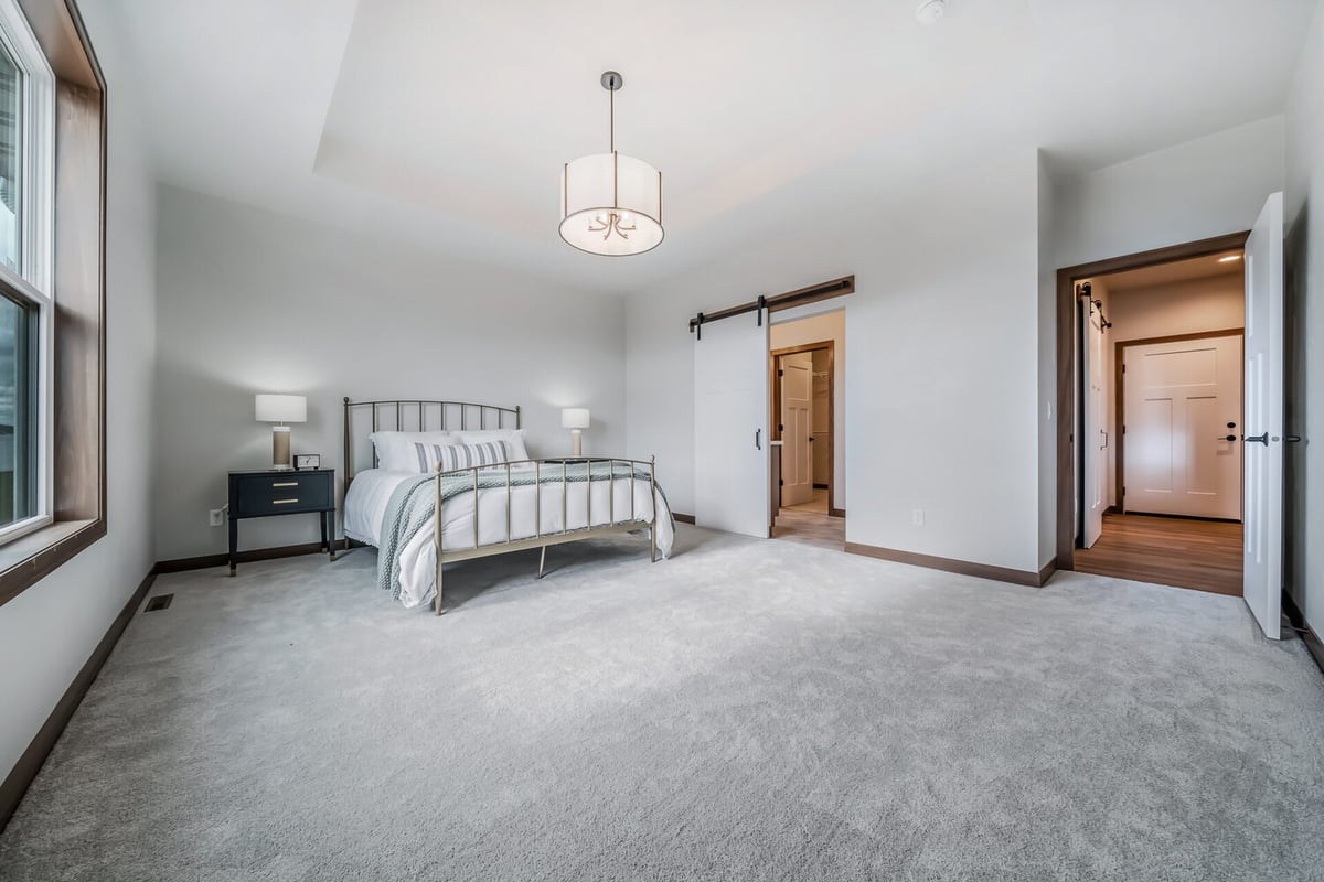 Primary bedroom with tray ceiling and barn door access in Midwest Design Homes custom home in Ledgeview, WI