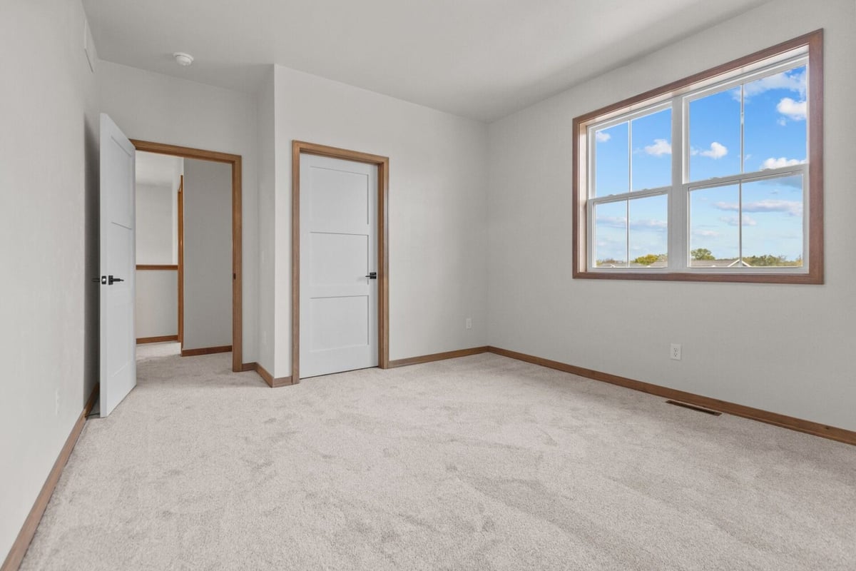 Carpeted bedroom with double doors and large window in a Midwest Design Homes custom home in De Pere, WI