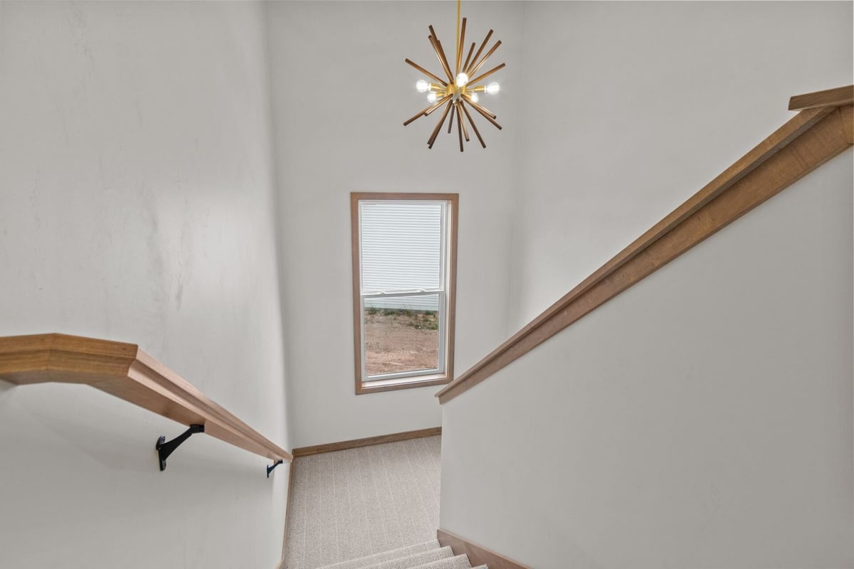 Carpeted staircase landing with large window and modern chandelier in a custom home by Midwest Design Homes in Neenah, WI