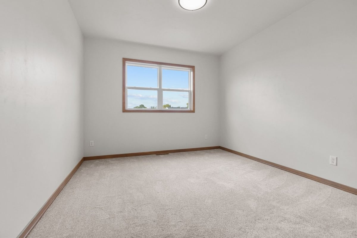 Empty guest bedroom with carpet flooring and single window in a Midwest Design Homes custom build in Ellington, WI