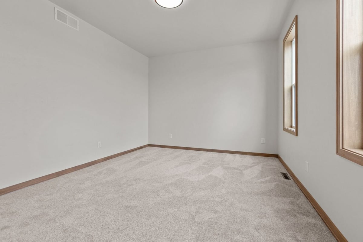 Minimalist bedroom with dual windows and carpet flooring in a Midwest Design Homes custom home in Ellington, WI